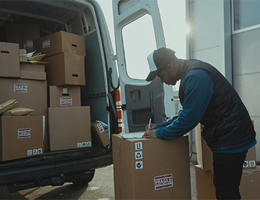 Man writing on a box in front of a van full of boxes | Freight Services